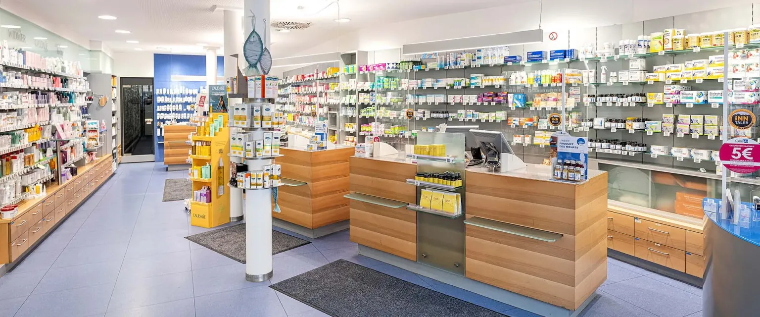 Heller Verkaufsraum der St. Anna-Apotheke mit Holz-Beratungstischen, Regalen und blauem Boden